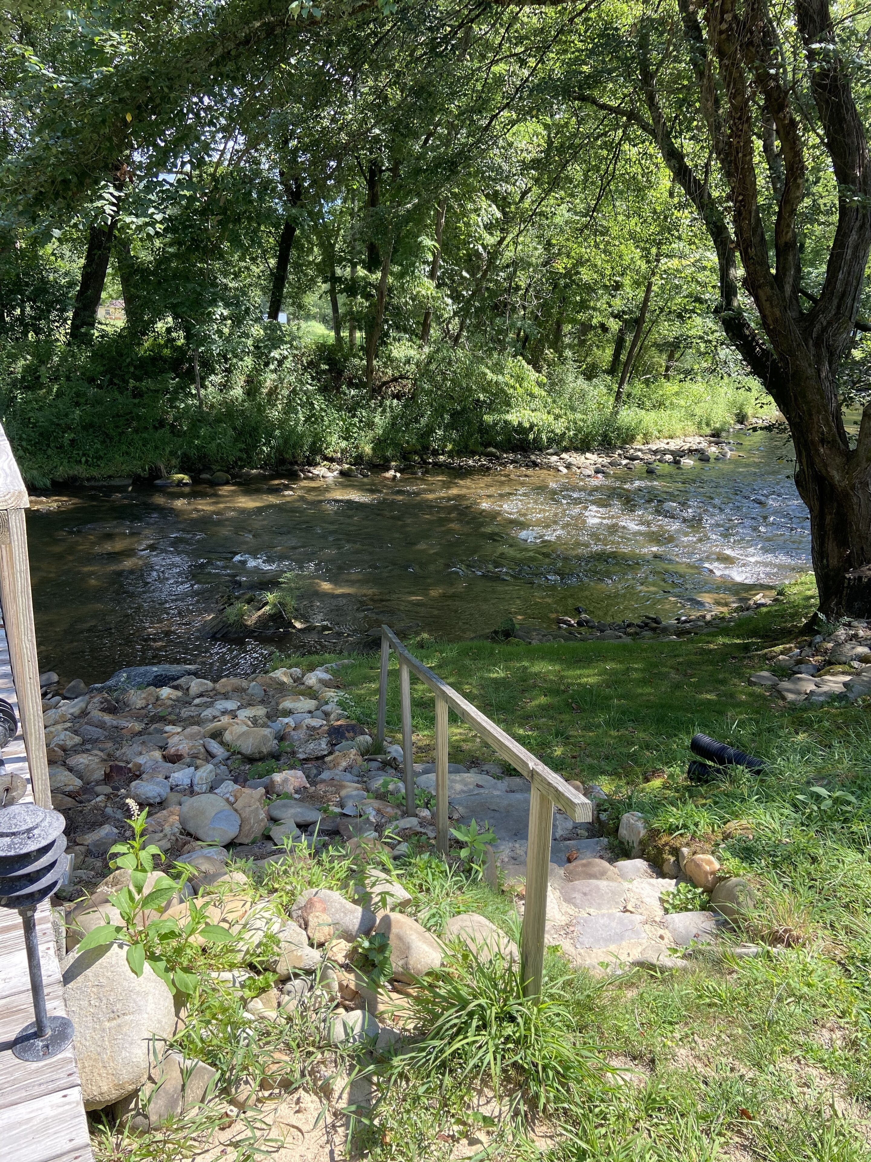 A riverside area with a wooden deck, a metal railing, and a stone pathway.