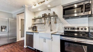 Una cocina moderna con electrodomésticos de acero inoxidable, armarios blancos y piso de madera.