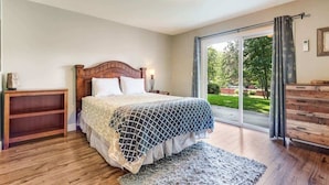 Ein Schlafzimmer mit einem hölzernen Bett, einem Nachttisch, einer Kommode und einer großen Schiebeglasdoor, die zu einem Garten führt.
