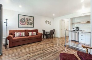 Ein Wohnzimmer mit einer Couch, einem Esstisch und Stühlen. Es gibt eine Küchenzeile mit einer Arbeitsfläche und Schränken.