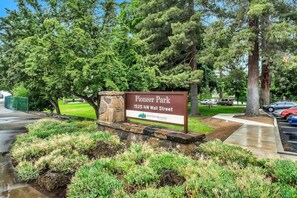 A sign for Pioneer Park at 1525 NW Wall Street, indicating a recreational area with a paved path and landscaped greenery.