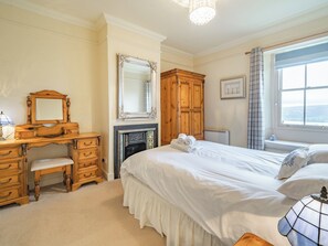 A bedroom with a wooden dresser, a large bed, a fireplace, and a window with curtains. - 2 bedroom accommodation in Watermillock (Watermillock)