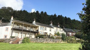 Ein großes, mehrgeschossiges Gebäude mit einer Steintreppe, die zu einem Balkon führt, umgeben von üppiger Vegetation und einem bewaldeten Hang.