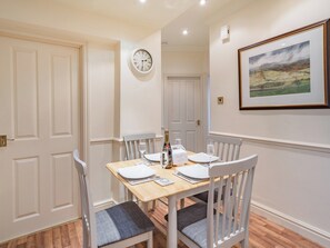 A dining area with a wooden table set for four, white chairs, a wall clock, and a framed landscape painting. - 2 bedroom accommodation in Watermillock (Watermillock)