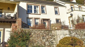 Ein zweistöckiges Haus mit Balkon, Steinmauer und Garten.