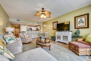 A spacious living room with a ceiling fan, a television, and a dining area with white furniture.
