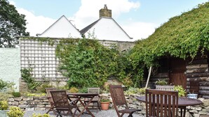A patio area with a table and chairs, surrounded by potted plants and a stone wall. - Foal Barn Cottages - Cobble Cottage-CC211117 (Spennithorne, near Leyburn)