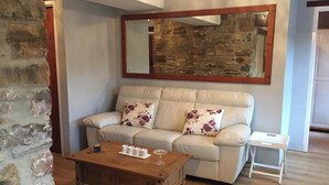 A living room with a stone wall, a beige sofa with floral cushions, a wooden coffee table, and a small white side table. - Foal Barn Cottages - Cobble Cottage-CC211117 (Spennithorne, near Leyburn)