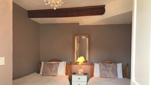 A bedroom with two single beds, a nightstand with a lamp, a mirror, and a wooden ceiling beam. - Foal Barn Cottages - Cobble Cottage-CC211117 (Spennithorne, near Leyburn)