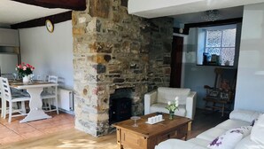 A living room with a stone fireplace, white furniture, and a dining area with a table and chairs. - Foal Barn Cottages - Cobble Cottage-CC211117 (Spennithorne, near Leyburn)