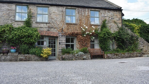 A stone house with a gravel driveway, a bench, and a small garden area. - Foal Barn Cottages - Cobble Cottage-CC211117 (Spennithorne, near Leyburn)