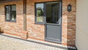 A brick building with two large windows and a door, a small garden area with a planter, and a visible outdoor light fixture. - Garden Cottage (Worcester)