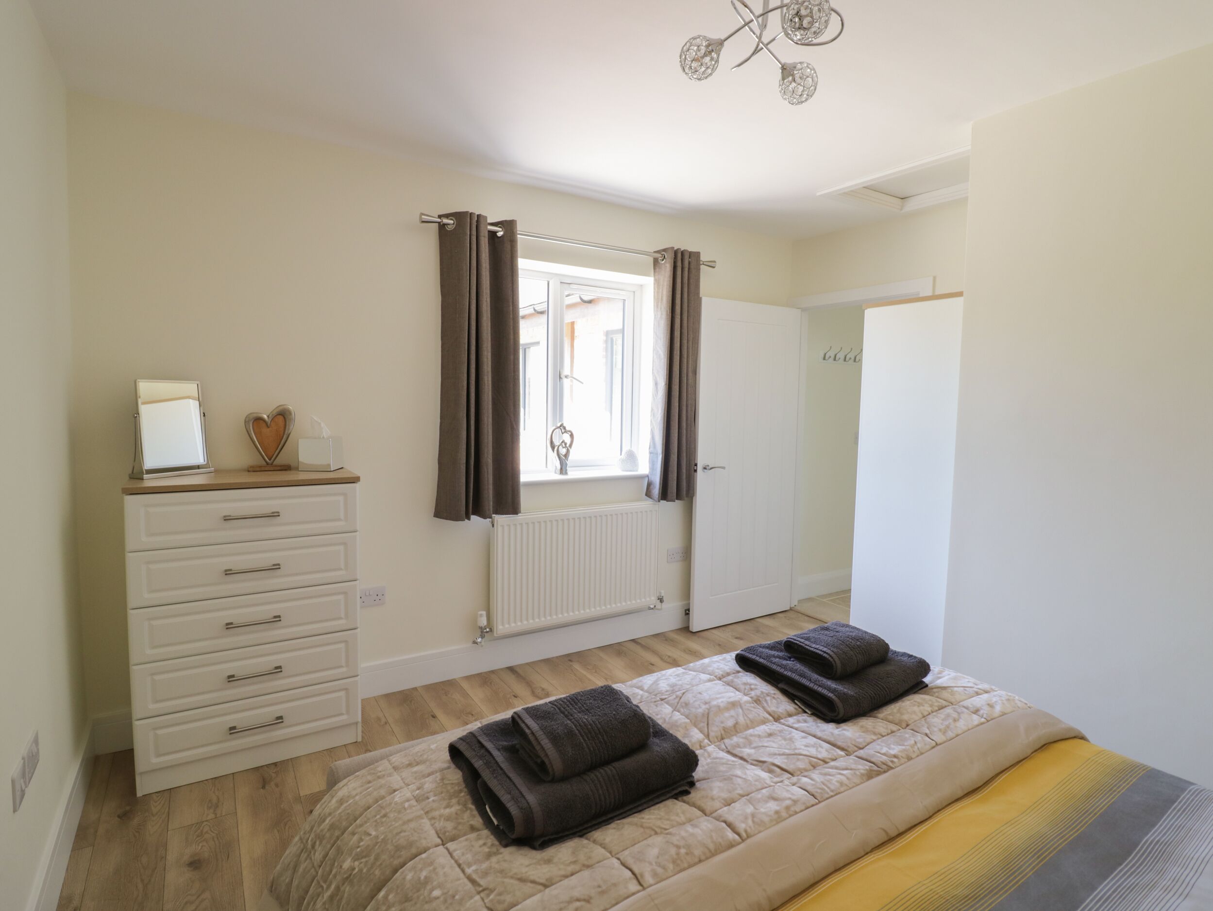 A bedroom with a bed, a dresser, a radiator, a window with curtains, and a door.