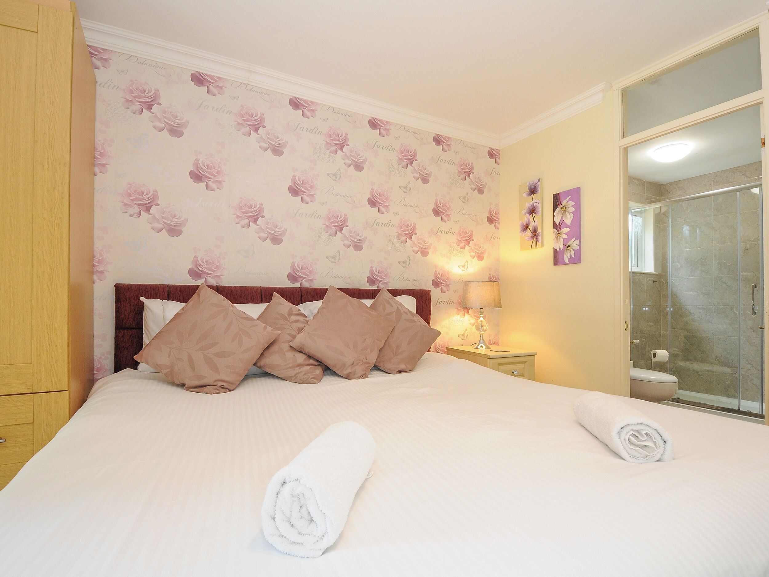 Une chambre d’hôtel comprenant un lit, des oreillers, une table de chevet, une lampe, un miroir et un espace douche.