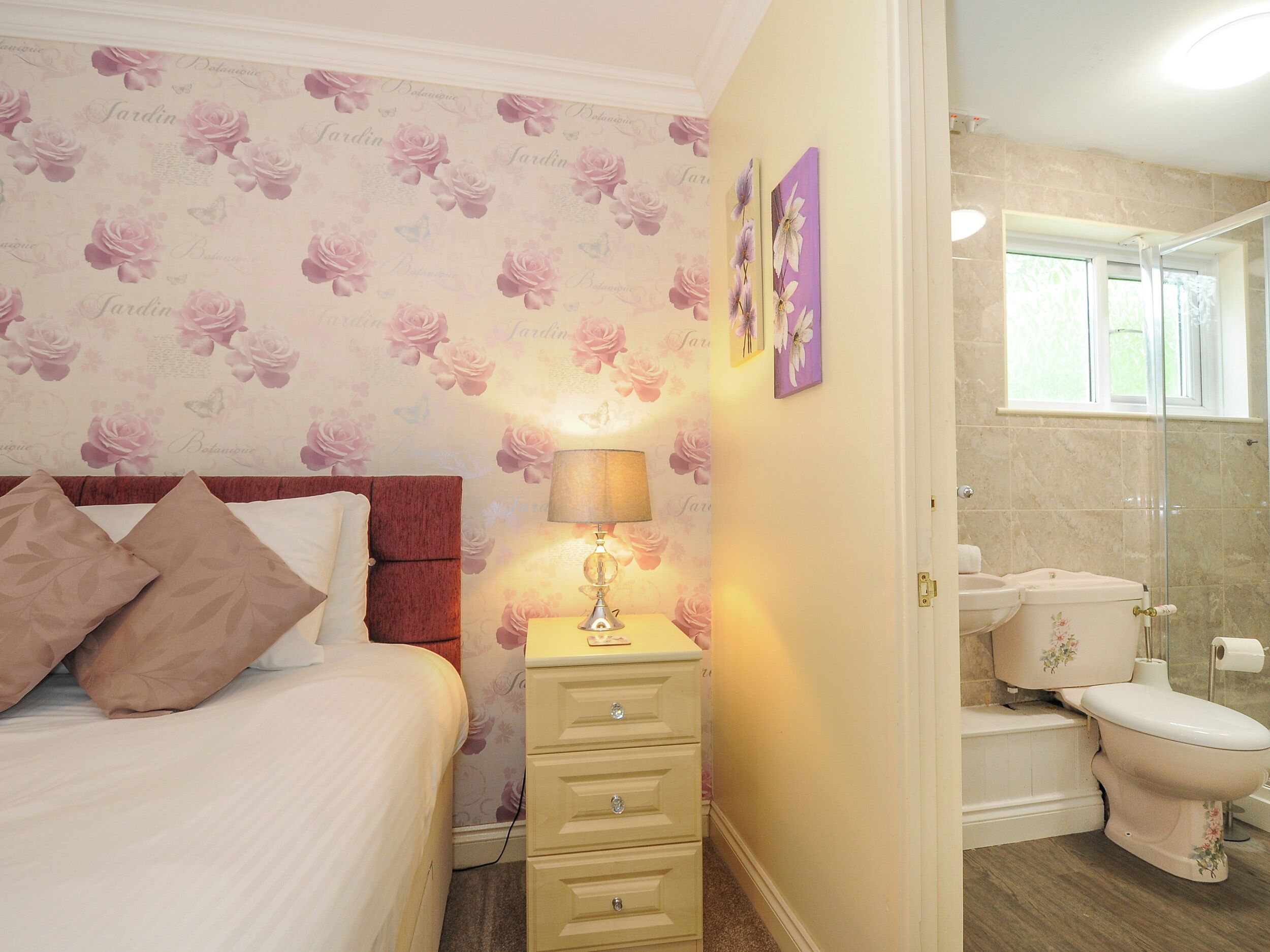 A bedroom with a bed, bedside table, lamp, and a bathroom with a toilet and shower.