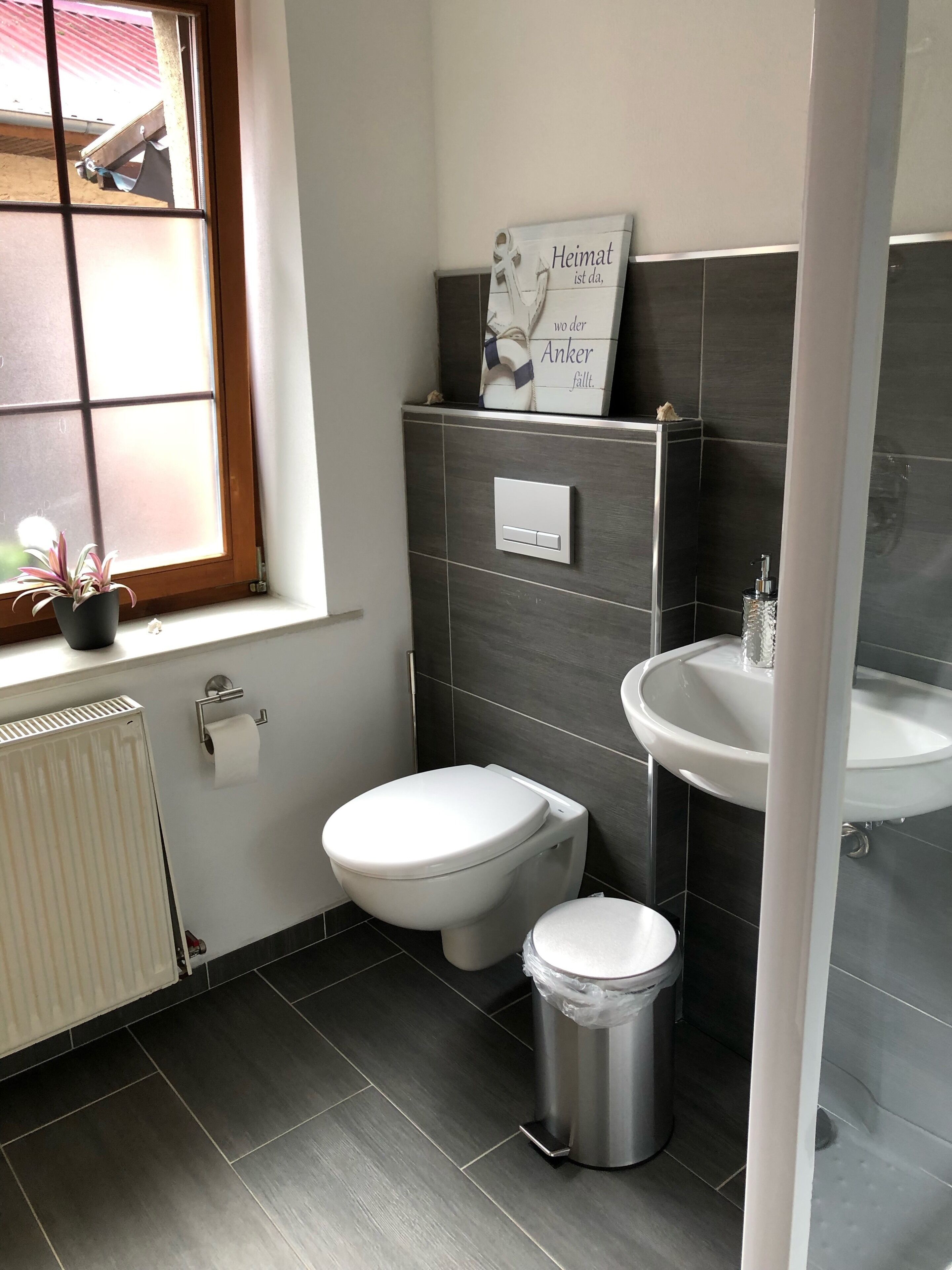 A modern bathroom with a toilet, bidet, and sink. There is a window with a view of the outside, and a sign on the wall.