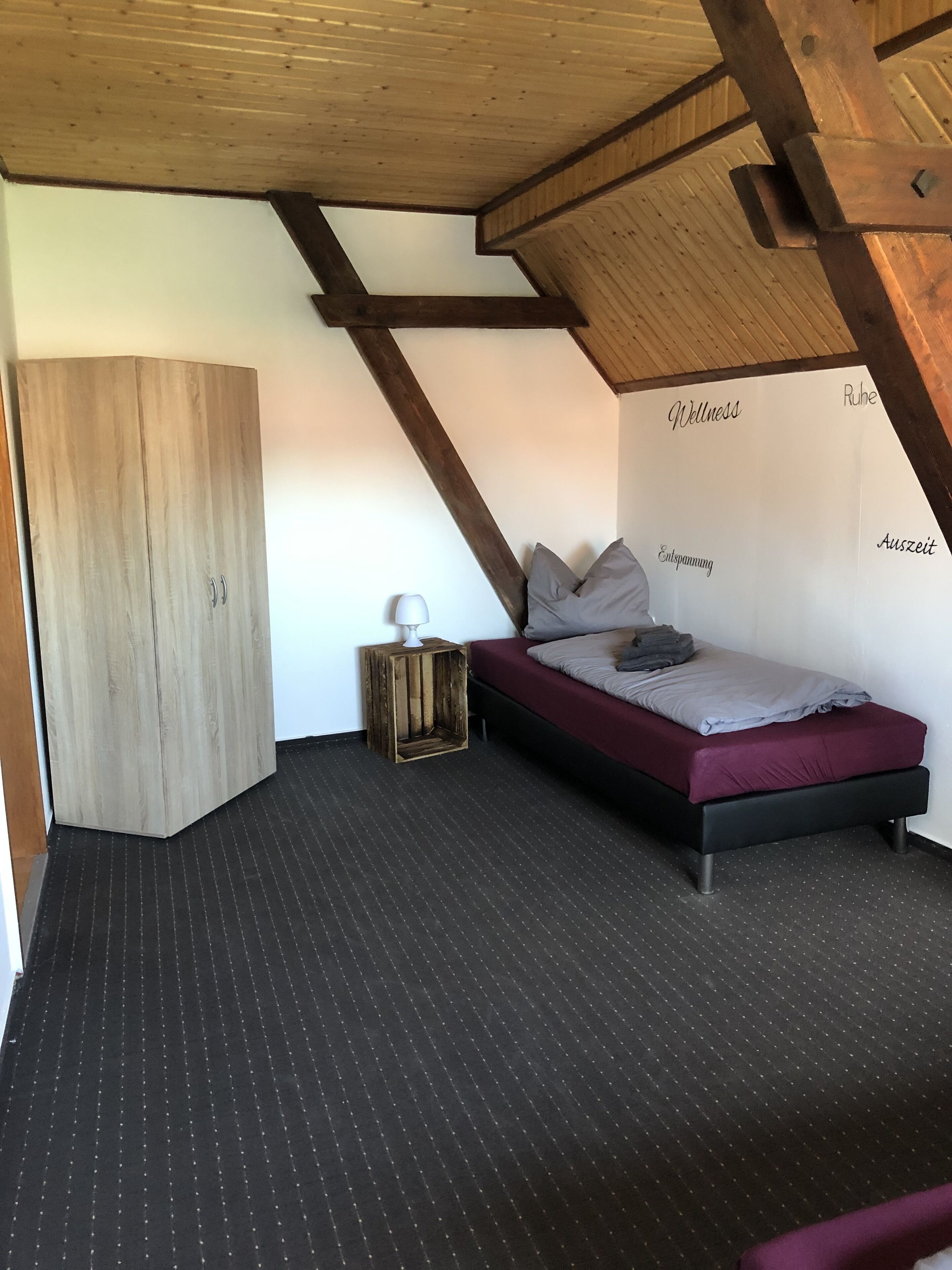 Ein Schlafzimmer mit schrägem Dach, einem Bett mit Kissen, einem Kleiderschrank und einem kleinen Nachttisch.