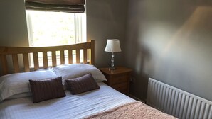 A bedroom with a wooden bed, two pillows, a bedside lamp, and a window with curtains. - Immaculate 3-bed Apartment in Kilkenny (Kilkenny)