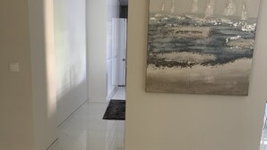 Un couloir orné d’un grand tableau représentant des voiliers, un tapis rond au sol et une porte donnant sur une autre pièce.