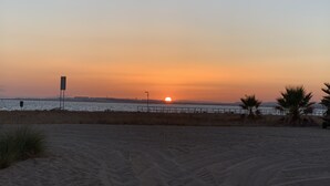 Une plage au coucher du soleil, avec un ciel dégagé, un premier plan sablonneux et une vue lointaine sur la mer.