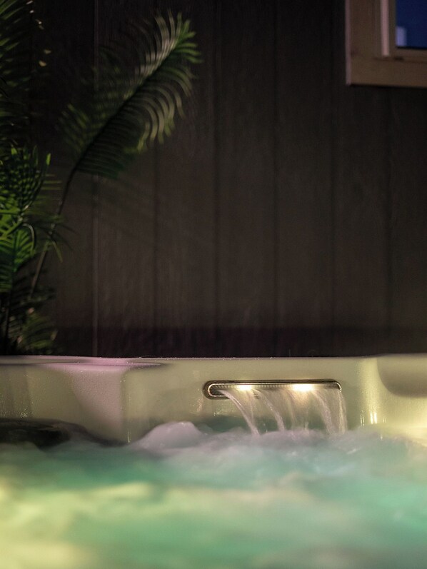 A hot tub with water flowing, surrounded by a wooden wall and a plant.