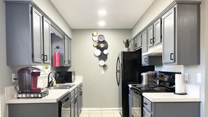 A compact kitchen with grey cabinets, a black refrigerator, a stove, and a coffee maker.