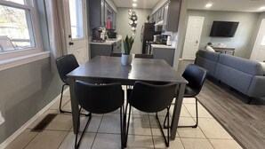 A modern kitchen with a dining area, a grey sofa, and a TV in the living room.