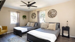 A bedroom with two beds, a ceiling fan, a small table, and a chair.