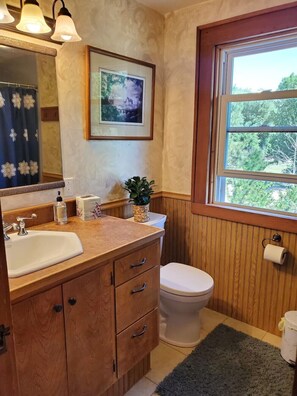 A bathroom with a wooden vanity, a sink, a toilet, a framed picture, and a window with a view of trees. - Rustic Farmhouse-Walk to Main Street Augusta  (Augusta,)