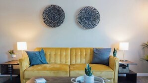 A living room with a yellow sofa, two side tables with lamps, and a coffee table with books and a plant. - Boho 3 Bed Condo Near ETSU 102 (Johnson City)