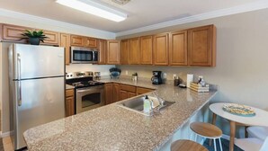 A modern kitchen with granite countertops, stainless steel appliances, wooden cabinets, and a bar area with stools. - Boho 3 Bed Condo Near ETSU 102 (Johnson City)