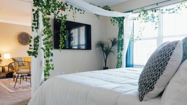 A bedroom with a bed, a TV mounted on the wall, and a window with curtains. - Boho 3 Bed Condo Near ETSU 102 (Johnson City)