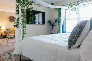 A bedroom with a bed, a TV mounted on the wall, and a window with curtains. - Boho 3 Bed Condo Near ETSU 102 (Johnson City)