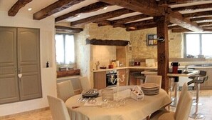 Un comedor rústico con vigas de madera a la vista, pared de piedra y cocina al fondo.