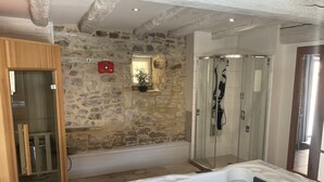 Un baño con pared de piedra, cabina de ducha de cristal, armario de madera y bañera de hidromasaje.