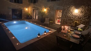 Una piscina con muro de piedra y zona de comedor con velas.