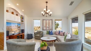 Uma sala de estar ampla com uma televisão grande, assentos confortáveis, um lustre e grandes janelas com vista para o deserto.