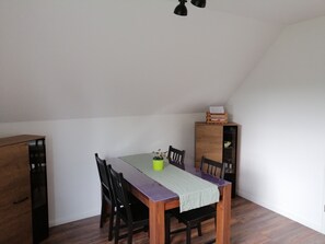 A dining area with a wooden table, four chairs, a green tablecloth, a yellow vase, and a wooden cabinet with a glass door.