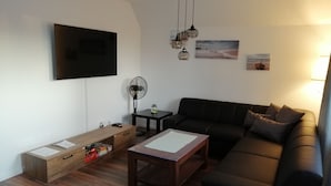 A modern living room with a black leather sofa, wooden coffee table, and a flat-screen TV mounted on the wall.