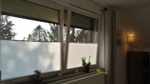 A room with a radiator, a window with blinds, a small table with a lamp, and a potted plant on the windowsill.