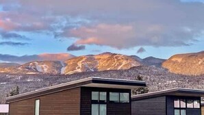 A modern building with a sloped roof, large windows, and a view of mountains. - Bring Fido | Pool & Hot Tub | Amazing Location (Whitefish)