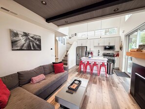 A modern living room with a grey sofa, red cushions, a coffee table, and a painting of a forest.