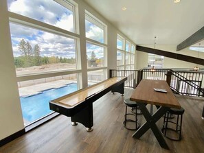 Una mesa de billar en una habitación amplia con ventanas grandes, un banco de madera y una zona de bar.