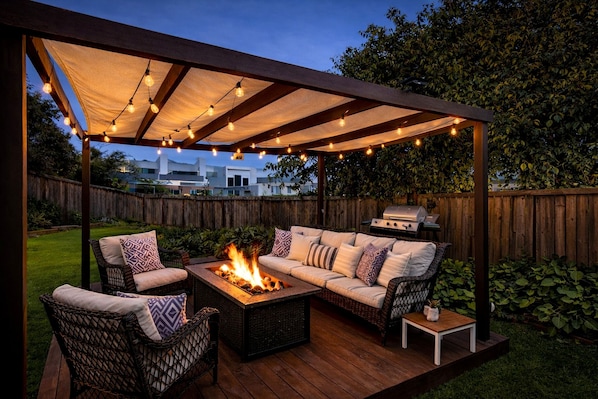 An outdoor patio with a fire pit, seating, and string lights.