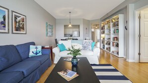 Un salon avec un canapé bleu, un canapé blanc, une table basse avec un livre, un vase de fleurs et une bibliothèque.