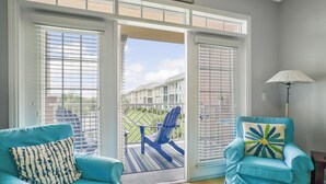 Une pièce avec un canapé bleu, un fauteuil bleu et une vue, à travers une porte vitrée, sur une terrasse où se trouve une chaise bleue.