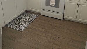 Una cocina con armarios blancos, estufa, microondas y un tapete estampado.