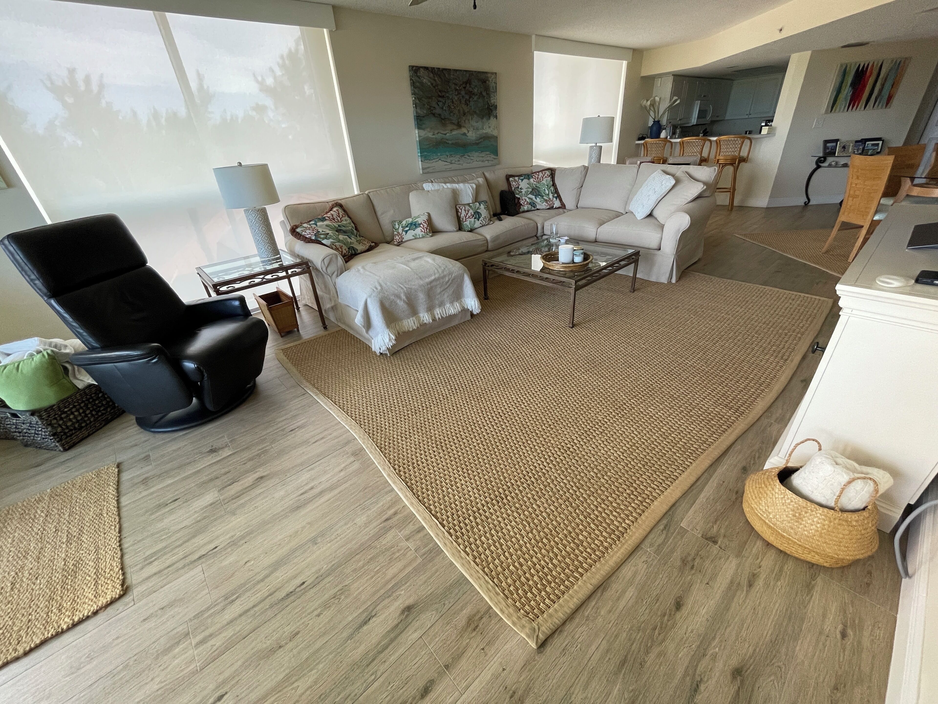 A modern living room with a sectional sofa, a black leather chair, a glass coffee table, and a woven rug.