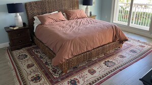 Un dormitorio con una cama grande, dos mesitas de noche con lámparas, una alfombra estampada y vistas al exterior con vegetación.