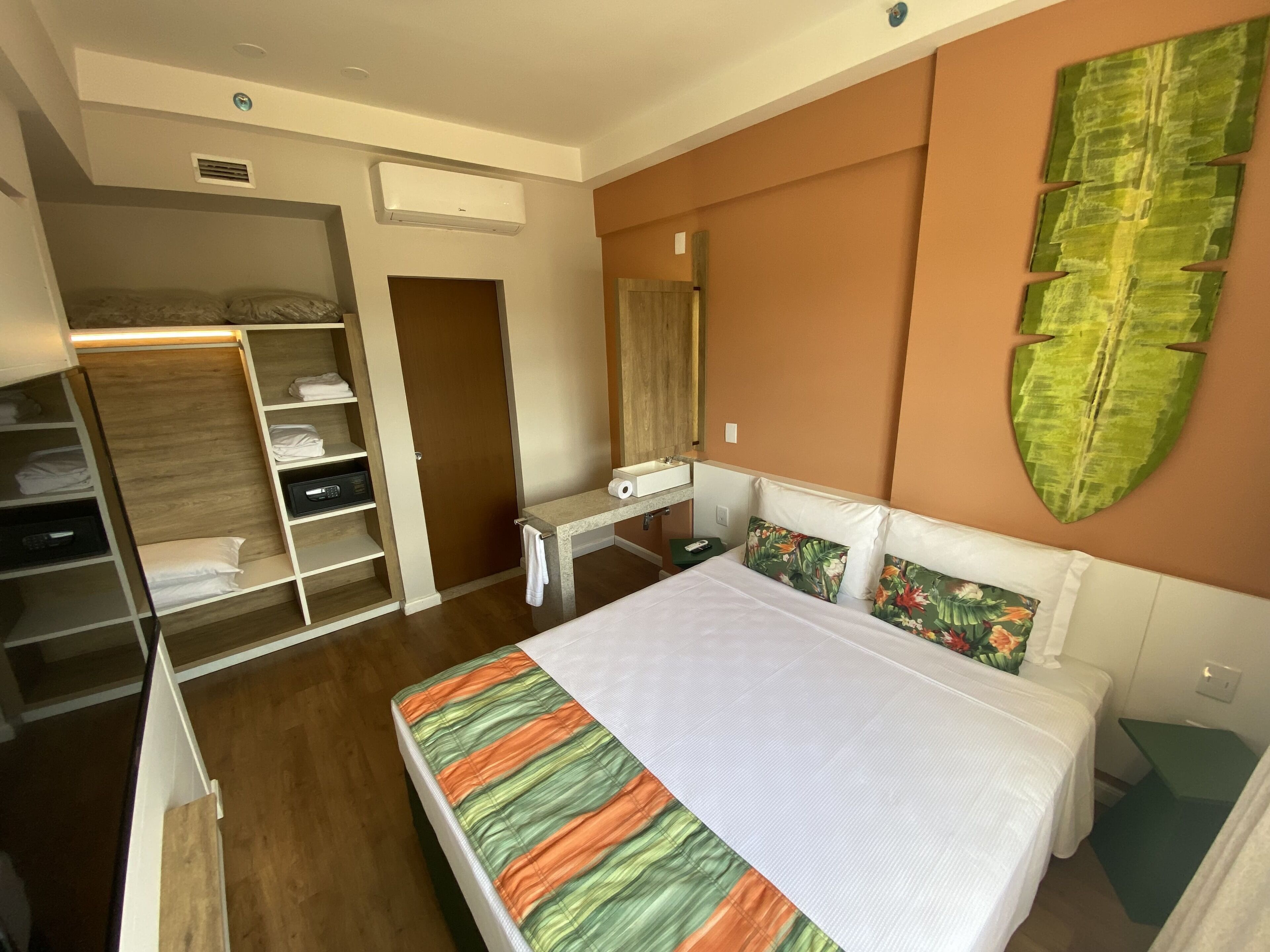 Quarto com cama, guarda-roupa, penteadeira e um espelho grande.